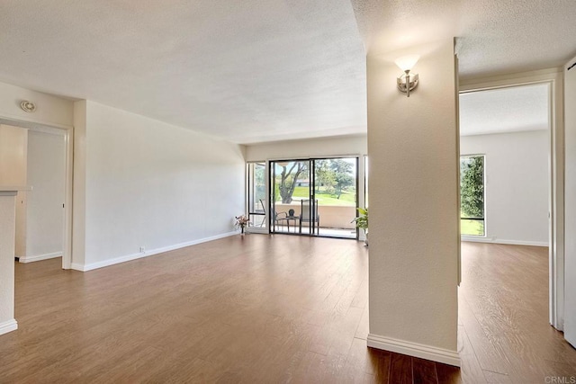 unfurnished living room with wood finished floors, baseboards, and a textured ceiling