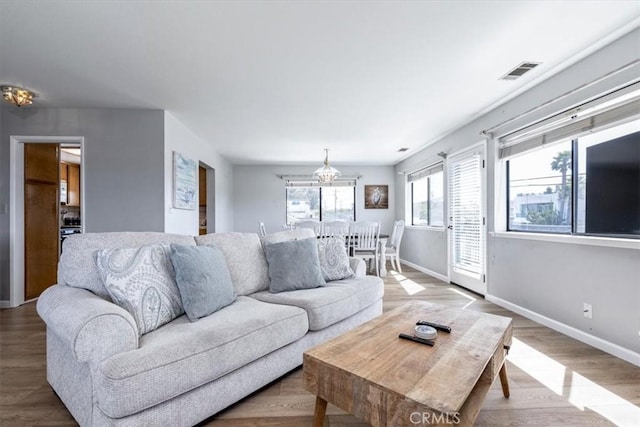 living area with baseboards, wood finished floors, visible vents, and an inviting chandelier
