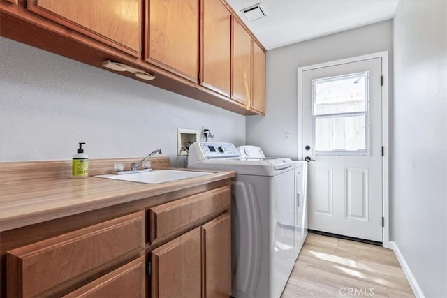 clothes washing area featuring light wood finished floors, visible vents, a sink, washer and dryer, and cabinet space