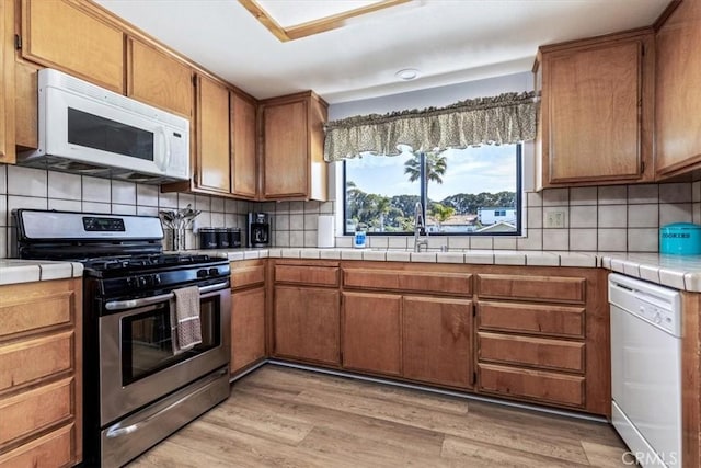 kitchen with a sink, backsplash, white appliances, brown cabinetry, and tile countertops