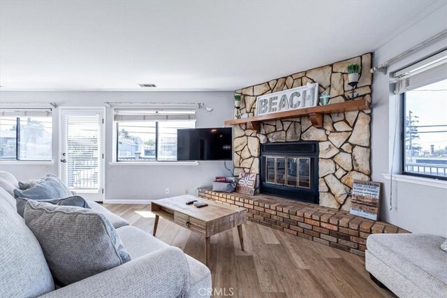 living area with visible vents, a stone fireplace, wood finished floors, and a healthy amount of sunlight
