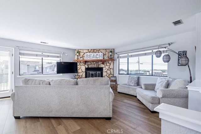 living area with wood finished floors, visible vents, and a stone fireplace