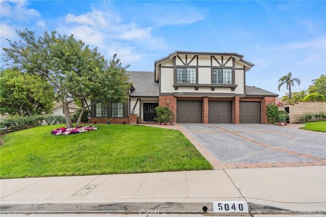 tudor house with a front lawn, stucco siding, driveway, brick siding, and a garage