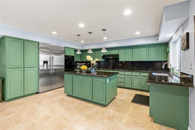 kitchen featuring green cabinetry, under cabinet range hood, a sink, built in refrigerator, and tasteful backsplash