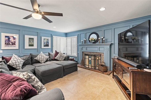 living room with a decorative wall, ceiling fan, a fireplace, ornamental molding, and recessed lighting
