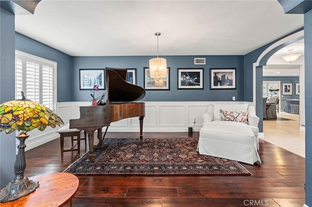 sitting room featuring hardwood / wood-style floors, visible vents, arched walkways, a decorative wall, and wainscoting