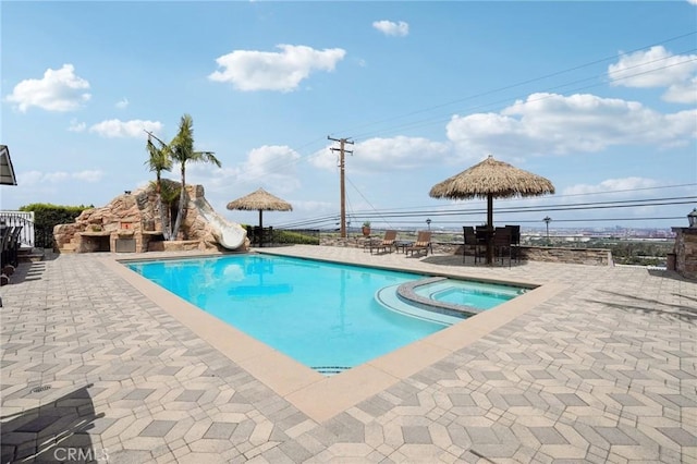 view of swimming pool with a pool with connected hot tub, a water slide, and a patio