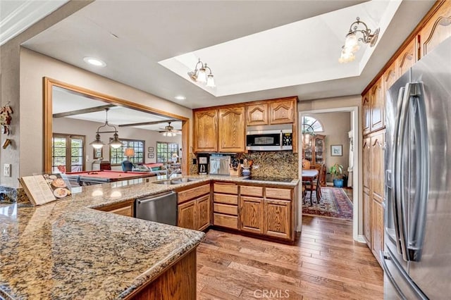 kitchen with light stone countertops, brown cabinets, tasteful backsplash, light wood-style flooring, and appliances with stainless steel finishes