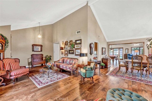 living area with crown molding, hardwood / wood-style floors, high vaulted ceiling, and visible vents