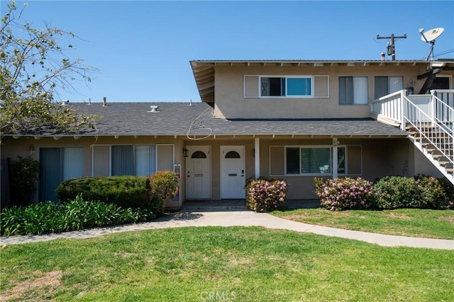 view of front of house featuring stucco siding, a front lawn, stairway, and roof with shingles