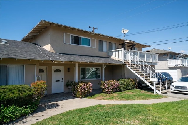view of front of property with stairway, a front lawn, roof with shingles, and stucco siding