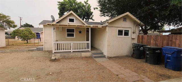 bungalow-style house featuring a porch, fence, and stucco siding