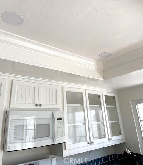 kitchen view of white microwave, white cabinetry, glass insert cabinets, and ornamental molding