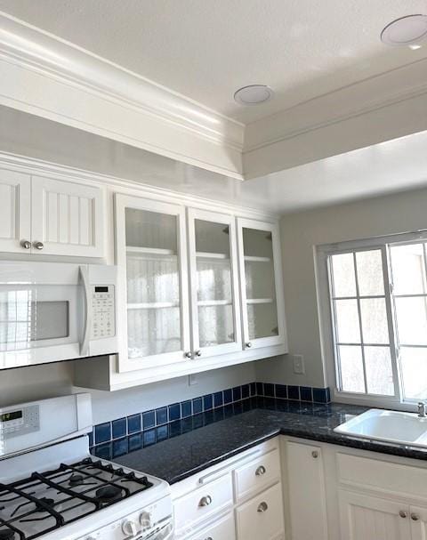 kitchen featuring white appliances, white cabinets, dark countertops, and crown molding