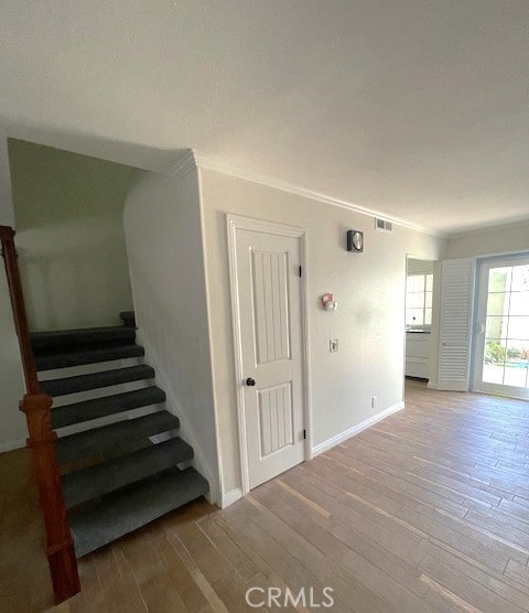 staircase with wood finished floors, baseboards, and ornamental molding