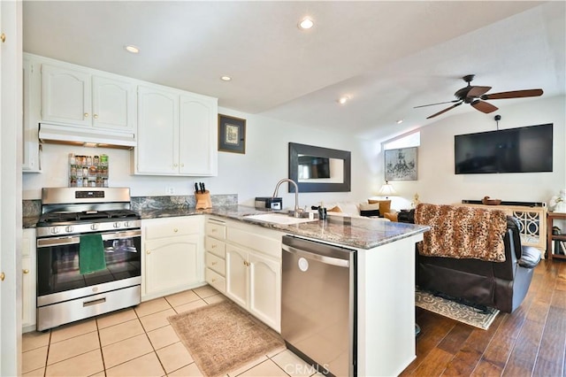kitchen with a sink, dark stone countertops, a peninsula, under cabinet range hood, and stainless steel appliances
