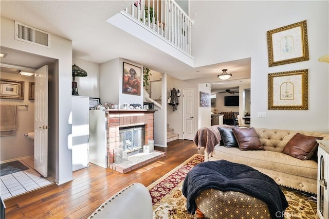 living room featuring visible vents, a brick fireplace, hardwood / wood-style flooring, baseboards, and stairs