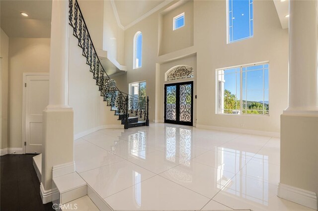 foyer entrance featuring ornate columns, a high ceiling, healthy amount of natural light, baseboards, and ornamental molding