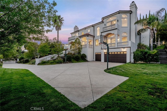 mediterranean / spanish house with a balcony, concrete driveway, an attached garage, a chimney, and stucco siding