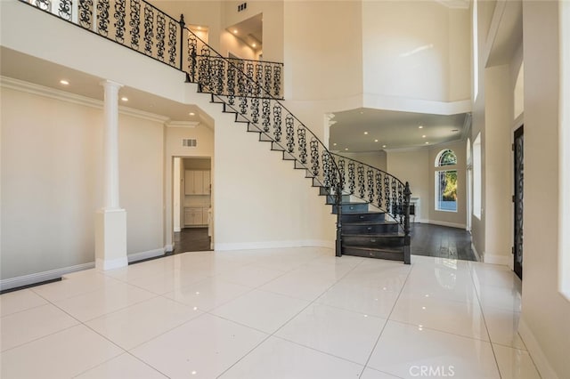 foyer featuring a towering ceiling, decorative columns, stairway, crown molding, and tile patterned flooring