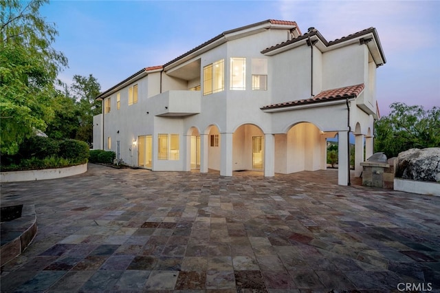 back of house featuring a tiled roof, stucco siding, decorative driveway, a patio, and a carport