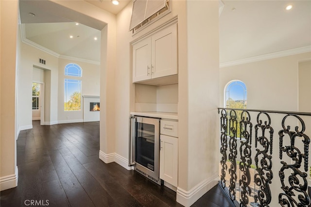 indoor dry bar featuring beverage cooler, ornamental molding, baseboards, dark wood-style flooring, and recessed lighting