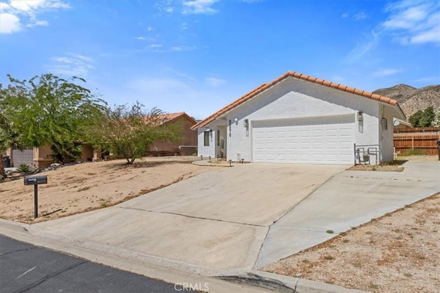 view of front facade with fence, a tiled roof, stucco siding, driveway, and a garage