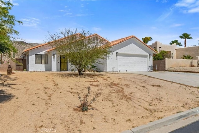 mediterranean / spanish-style home with stucco siding, an attached garage, fence, and a tile roof