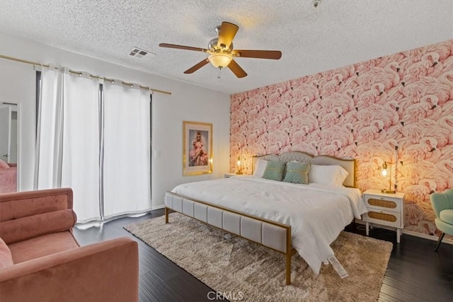 bedroom with a textured ceiling, wood finished floors, visible vents, and ceiling fan