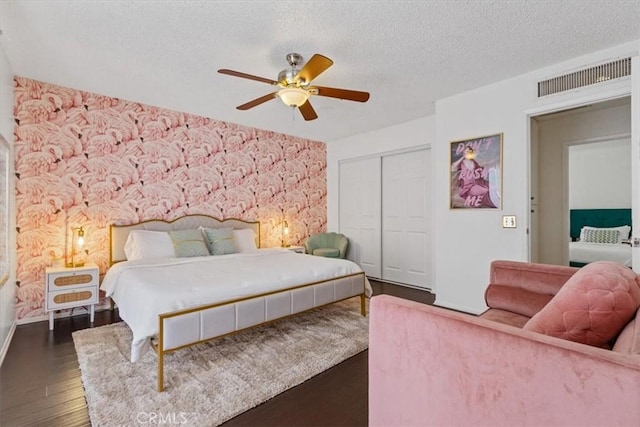 bedroom with dark wood-style floors, a textured ceiling, visible vents, a closet, and ceiling fan