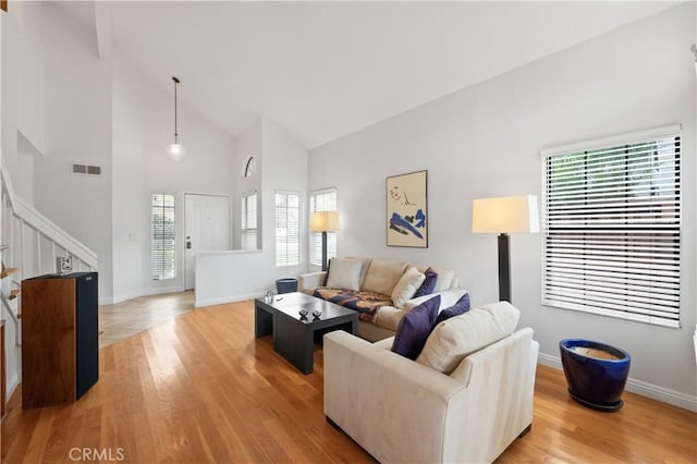 living area featuring stairway, visible vents, a healthy amount of sunlight, and high vaulted ceiling