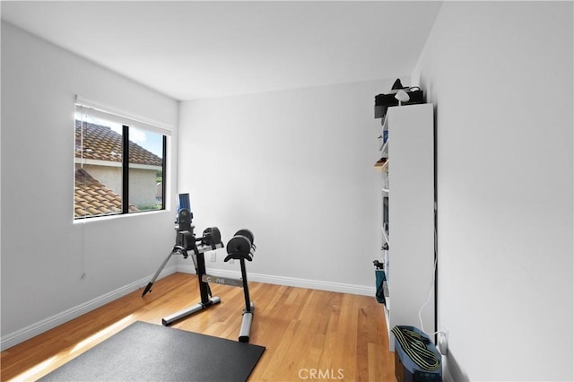 exercise room with baseboards and light wood-style flooring