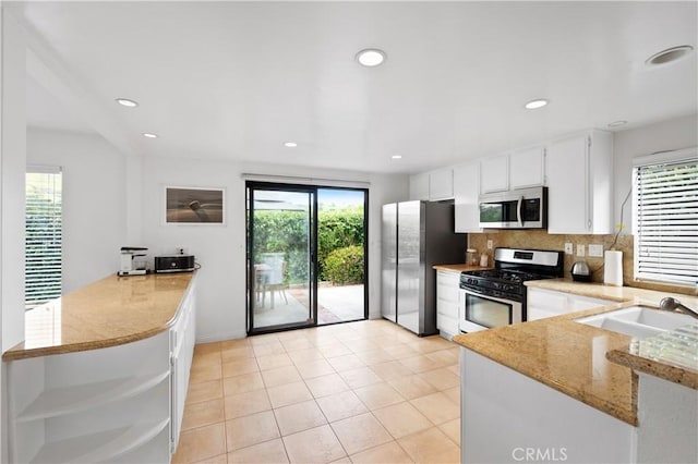 kitchen with white cabinetry, a sink, appliances with stainless steel finishes, a peninsula, and backsplash