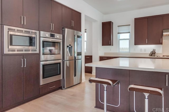 6222 Artisan Way, San Diego, CA 92130 - kitchen with a kitchen bar, dark brown cabinets, light countertops, light wood-style floors, and stainless steel appliances