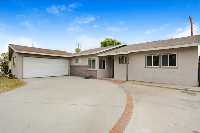 ranch-style house with stucco siding, a garage, concrete driveway, brick siding, and roof with shingles