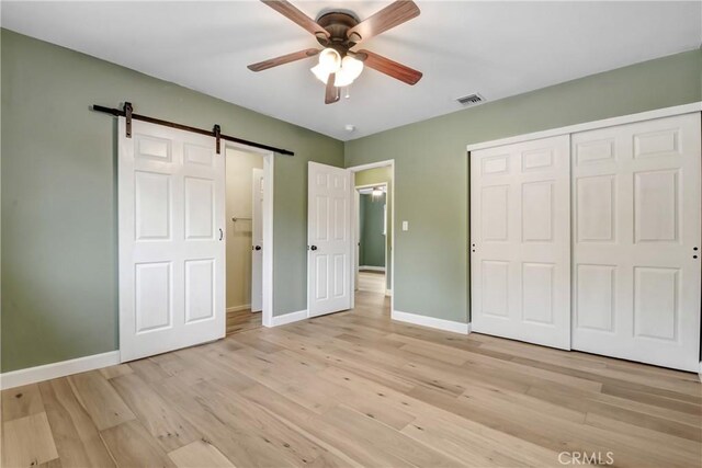 unfurnished bedroom with a barn door, baseboards, and light wood-style flooring