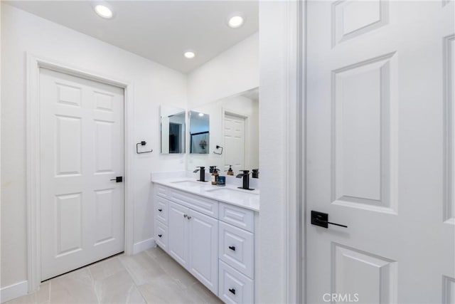 bathroom with baseboards, a sink, double vanity, and recessed lighting