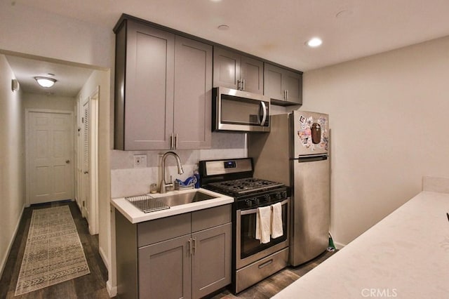 kitchen with stainless steel appliances, a sink, gray cabinets, light countertops, and dark wood-type flooring