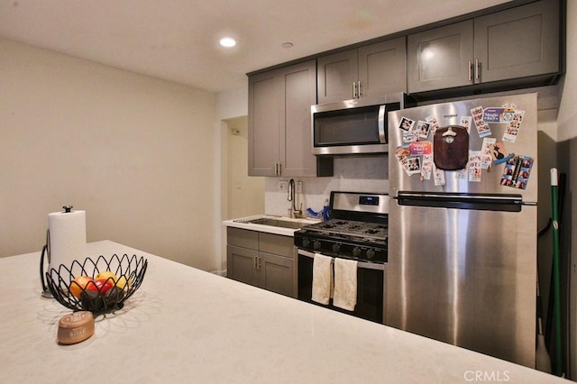 kitchen featuring recessed lighting, stainless steel appliances, light countertops, gray cabinets, and a sink