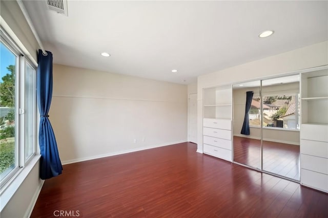 unfurnished bedroom featuring wood finished floors, visible vents, and multiple windows