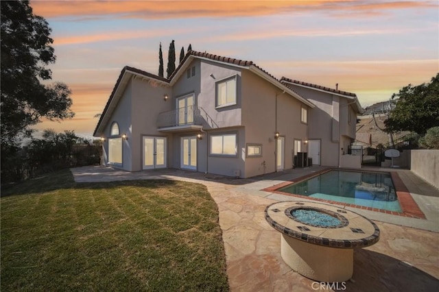 back of property featuring french doors, a patio area, a lawn, a balcony, and stucco siding