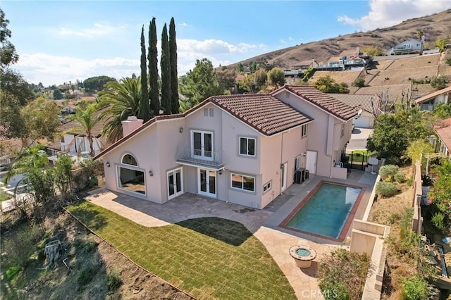 rear view of property with a patio area, a lawn, an outdoor pool, and stucco siding