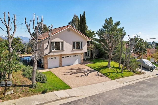 traditional-style home featuring a tile roof, an attached garage, a front yard, stucco siding, and decorative driveway
