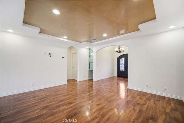 unfurnished living room with baseboards, arched walkways, recessed lighting, and a raised ceiling