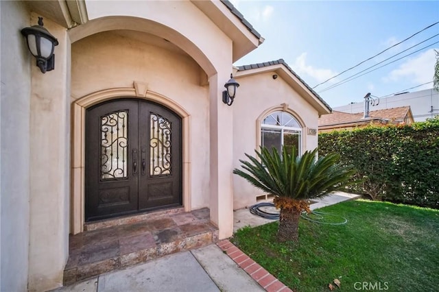 entrance to property with stucco siding, a lawn, and french doors