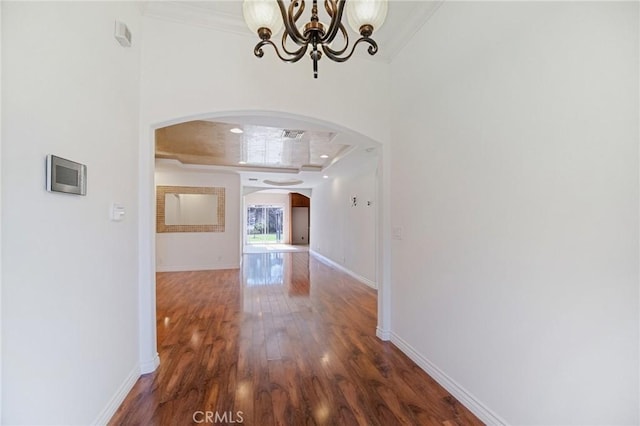 hall featuring arched walkways, wood finished floors, ornamental molding, and an inviting chandelier