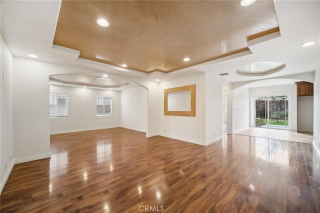 spare room with arched walkways, baseboards, hardwood / wood-style flooring, and a tray ceiling