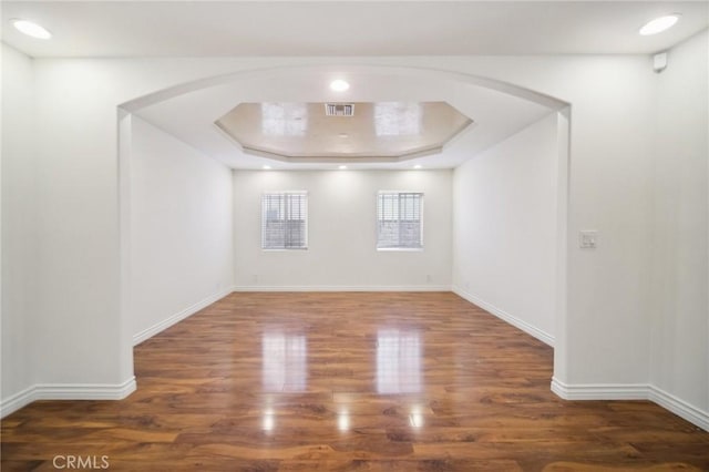 unfurnished room featuring wood finished floors, visible vents, and arched walkways