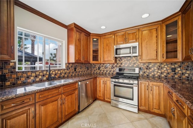 kitchen featuring a sink, dark stone counters, light tile patterned flooring, brown cabinets, and appliances with stainless steel finishes