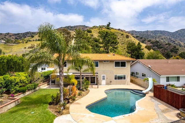 view of pool featuring fence, a water slide, a mountain view, and a patio area